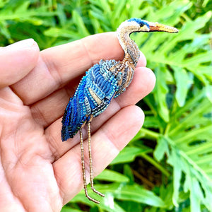 embroidered blue heron pin featuring thread and beads in varying shades of blue and tan, two long skinny legs made from tiny brown glass beads