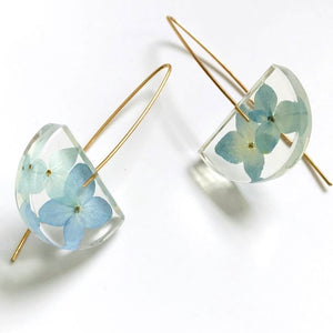 blue hydrangae earrings with two flowers floating in a half moon shaped clear resin drop and finished with long gold ear hooks